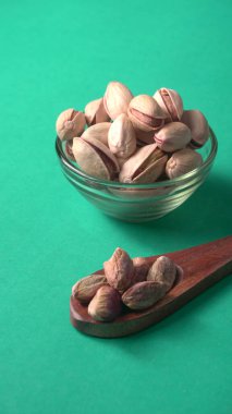 Kahverengi ahşap kaşık ve cam kavanozla süslenmiş fıstıklar veya Pista fındıkları. Yeşil arka plan, üst manzara. Düz yatıyordu.