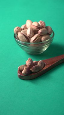 Kahverengi ahşap kaşık ve cam kavanozla süslenmiş fıstıklar veya Pista fındıkları. Yeşil arka plan, üst manzara. Düz yatıyordu.