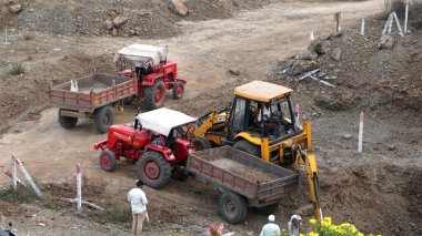 INDIA - 24 Ocak 2022: inşaat tarafında taş ve zemin taşıyan traktörlerdeki işçiler. Hava görünümü.