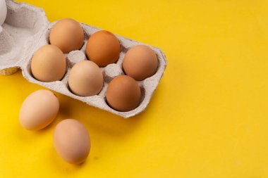 Sarı arka planda karton kutuda çiğ yumurta.