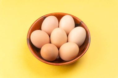 Sarı arka planda ahşap bir kase tavuk yumurtası, yakın çekim. 