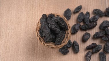 Tahta masanın üzerinde kurumuş siyah hurmalardan oluşan hasır sepetin yakınına.