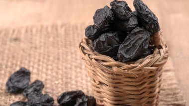 Tahta masanın üzerinde kurumuş siyah hurmalardan oluşan hasır sepetin yakınına.
