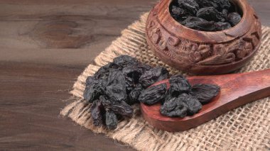 Çamur kase ve tahta kaşık kurutulmuş siyah hurmalar çuval, ahşap arka plan