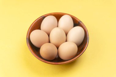 Sarı arka planda ahşap bir kase tavuk yumurtası, yakın çekim. 