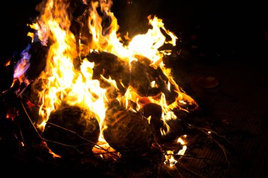 Kamp alanının karanlık zemininde kamp ateşinin kırmızı alevleri. Hava bulutlu, arka planda yakacak odunları olan kamp ateşi. Kamp havasını gevşetin, alçak açılı.