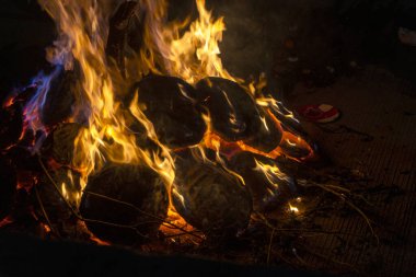 Kamp alanının karanlık zemininde kamp ateşinin kırmızı alevleri. Hava bulutlu, arka planda yakacak odunları olan kamp ateşi. Kamp havasını gevşetin, alçak açılı.