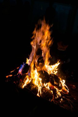 Kamp alanının karanlık zemininde kamp ateşinin kırmızı alevleri. Hava bulutlu, arka planda yakacak odunları olan kamp ateşi. Kamp havasını gevşetin, alçak açılı.