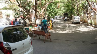 INDIA - 08 Mayıs 2020: Gündüz sebze pazarı ile caddede duran kalabalık, yeşil ağaçlı park halindeki araba 