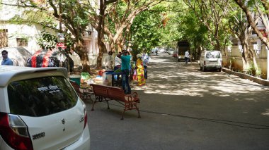 INDIA - 08 Mayıs 2020: Gündüz sebze pazarı ile caddede duran kalabalık, yeşil ağaçlı park halindeki araba 