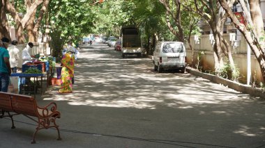 INDIA - 08 Mayıs 2020: Gündüz sebze pazarı ile caddede duran kalabalık, yeşil ağaçlı park halindeki araba 