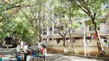 INDIA - 08 Mayıs 2020: Gündüz sebze pazarı ile caddede duran kalabalık, yeşil ağaçlı park halindeki araba 