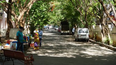 INDIA - 08 Mayıs 2020: Gündüz sebze pazarı ile caddede duran kalabalık, yeşil ağaçlı park halindeki araba 