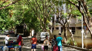 INDIA - 08 Mayıs 2020: Gündüz sebze pazarı ile caddede duran kalabalık, yeşil ağaçlı park halindeki araba 