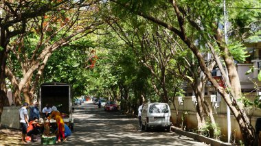 INDIA - 08 Mayıs 2020: Gündüz sebze pazarı ile caddede duran kalabalık, yeşil ağaçlı park halindeki araba 