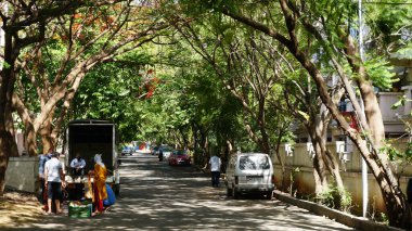 INDIA - 08 Mayıs 2020: Gündüz sebze pazarı ile caddede duran kalabalık, yeşil ağaçlı park halindeki araba 