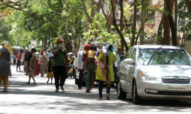 INDIA - 08 Mayıs 2020: Yeşil ağaçların gölgesinde park etmiş arabalarla eski caddenin yanından geçen kalabalık  