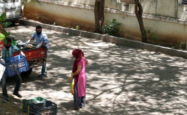 INDIA - 08 Mayıs 2020: Gündüz sebze pazarı ile caddede duran kalabalık, yeşil ağaçlı park halindeki araba 