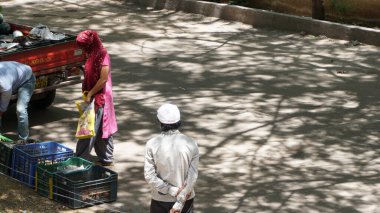 INDIA - 08 Mayıs 2020: Gündüz sebze pazarı ile caddede duran kalabalık, yeşil ağaçlı park halindeki araba 