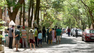 INDIA - 08 Mayıs 2020: Yeşil ağaçların gölgesinde park etmiş arabalarla eski caddenin yanından geçen kalabalık  