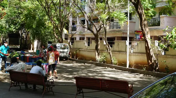 INDIA - 08 Mayıs 2020: Gündüz sebze pazarı ile caddede duran kalabalık, yeşil ağaçlı park halindeki araba 