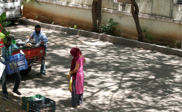 INDIA - 08 Mayıs 2020: Gündüz sebze pazarı ile caddede duran kalabalık, yeşil ağaçlı park halindeki araba 