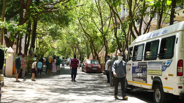 INDIA - 08 Mayıs 2020: Yeşil ağaçların gölgesinde park etmiş arabalarla eski caddenin yanından geçen kalabalık  