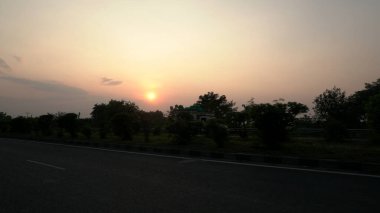 Gün batımında güzel gökyüzü altında yeşil bitkilerle çevrili boş Hint yolu. 