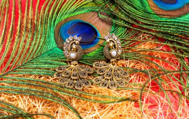 Beautiful earrings with peacock feather on red background 