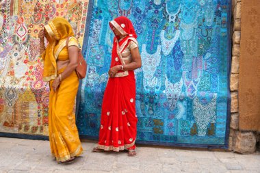 People walking near traditional colorful carpets on street of Indian city