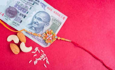 Traditional Indian jewelry with rice, peanuts and money banknotes on red background