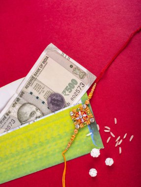 Traditional Indian jewelry with rice, greeting card and money banknotes on red background