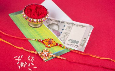 Traditional Indian jewelry with rice, spice, greeting card and money banknotes on red background