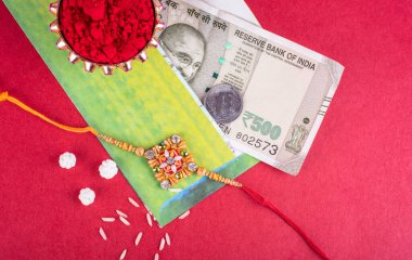 Traditional Indian jewelry with rice, spice, greeting card and money banknotes on red background
