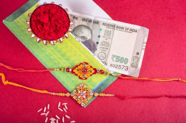Traditional Indian jewelry with rice, spice, greeting card and money banknotes on red background