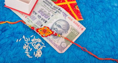 Traditional Indian jewelry with rice, envelope and money banknotes on blue background