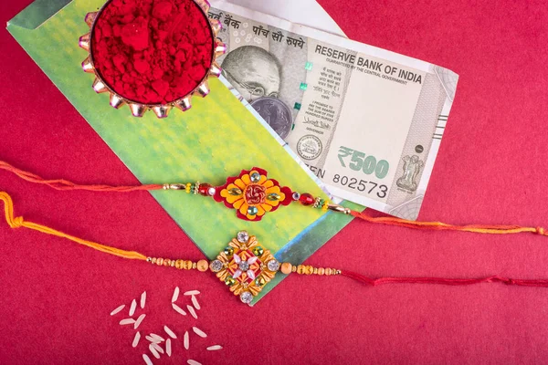 Traditional Indian jewelry with rice, spice, greeting card and money banknotes on red background