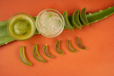 Aloe vera leaves with cosmetic cream and juice in bowls on orange background