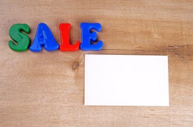 'Sale' word and white empty paper on wooden background