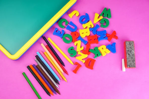 English alphabet letters, colorful pencils and childish school blackboard on pink background. Back to school. Education concept