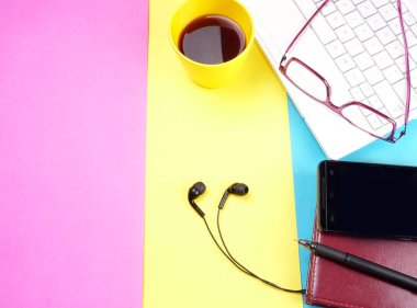 Laptop, glasses, coffee cup, notebook, pencil, glasses, smartphone with headphones on colorful background