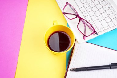 Glasses, smartphone, notebook, pencil and coffee cup on colorful background