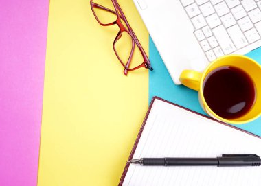 Glasses, smartphone, notebook, pencil and coffee cup on colorful background