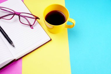 Notebook, pencil, glasses and coffee cup on colorful background
