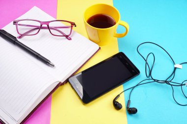 Notebook, pencil, glasses, coffee cup and smartphone with headphones on colorful background