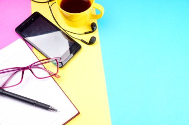 Notebook, pencil, glasses, coffee cup and smartphone with headphones on colorful background