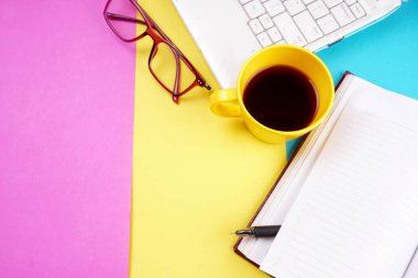 Glasses, smartphone, notebook, pencil and coffee cup on colorful background