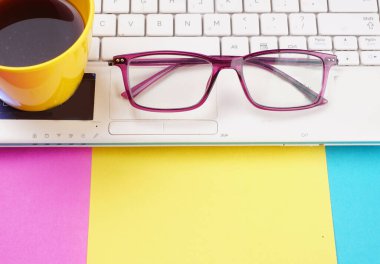 Glasses, smartphone and coffee cup on colorful background