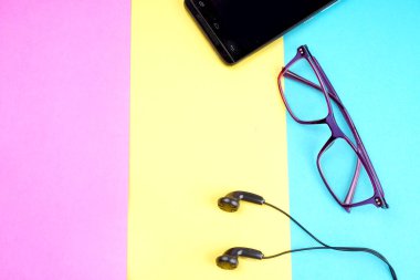 Glasses, smartphone with headphones on colorful background