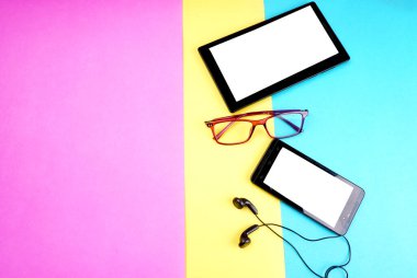 Glasses, digital tablet and smartphone with headphones on colorful background